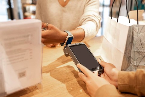 A customer uses a smartwatch for a contactless payment at a cosmetics store counter. A cashier