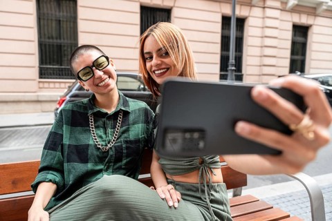 A Colombian lesbian couple captures a joyful selfie on a city bench, celebrating diversity and love