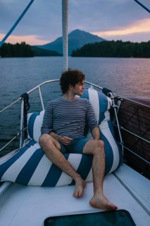 A serene afternoon on a sailboat, capturing a man relaxing against striped cushions. Surrounded by