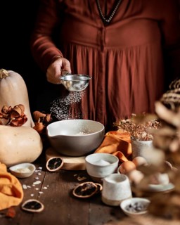A cozy autumn scene of a homemade pumpkin cake being prepared. A person sprinkles ingredients into