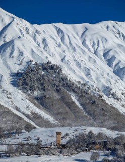 A picturesque winter scene featuring snow-covered mountains and a historic tower, surrounded by
