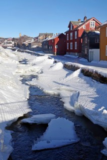 Snow-covered cityscape with an ice-covered river and traditional wooden houses, Røros, mining town,