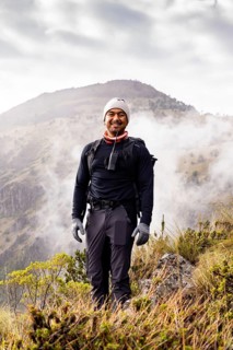 A hiker smiling in a scenic landscape with misty mountains in the background, wearing hiking gear