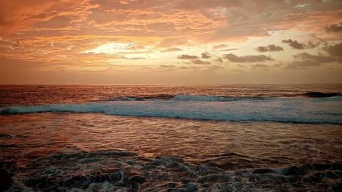 Waves break in the atmospheric light of sunset with an intensely glowing orange sky, Ponta do Sol,