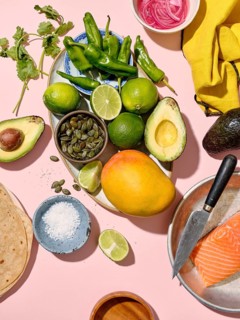 Top view of a vibrant array of taco ingredients spread on a pink backdrop, including green chilies,