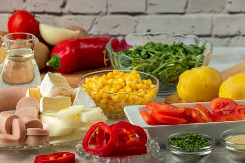 Preparation for salad with potatoes, tomatoes, peppers, sausage, corn, onions, cheese and arugula
