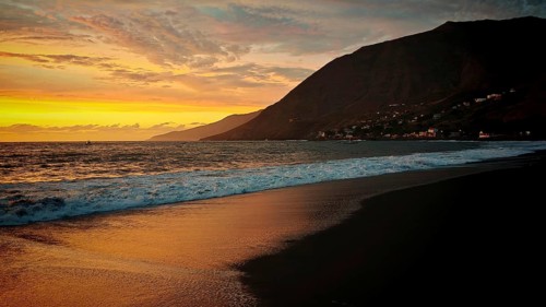 Romantic sunset on the beach with volcanic sand in front of mountains with shade and light at the