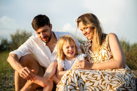 A joyful family sits together on an Italian beach, basking in the sun. The parents share a tender