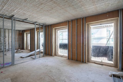 A bright, empty room under renovation, showcasing exposed metal wall frames and large window