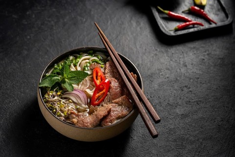 Taditional Vietnamese Beef Pho Noodle Soup served in a stylish dark bowl, garnished with slices of
