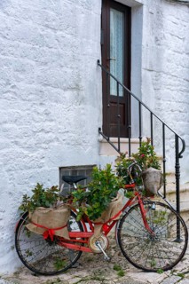 Charming red bicycle with flower baskets parked near the whitewashed stone walls of a traditional