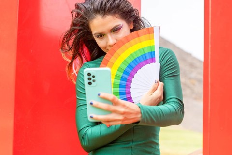 A woman, embodying LGBTQIA+ pride, takes a selfie with a rainbow fan, symbolizing diversity and