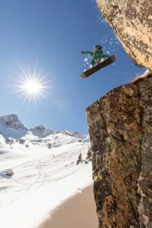 A snowboarder executes a thrilling jump off a rocky cliff, soaring through clear blue skies in a