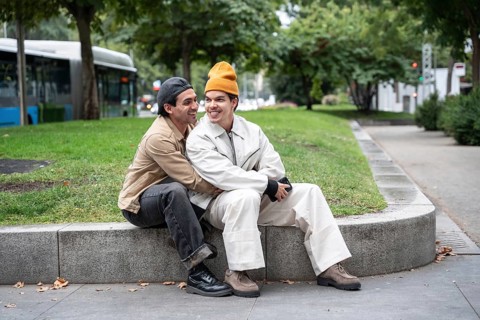 A joyful Colombian gay couple sitting closely on a park bench, enjoying each other's company on a
