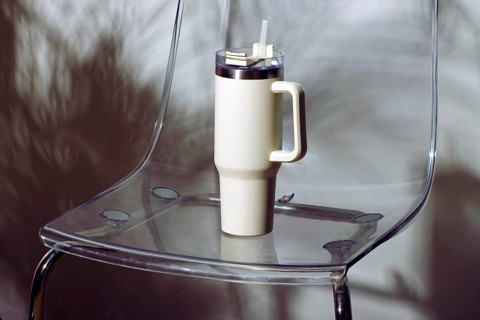 A stylish thermal mug with a handle and straw placed on a transparent acrylic chair, creating a