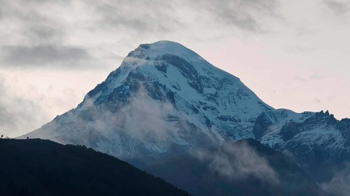A snow-covered mountain Kazbek at dusk surrounded by clouds, Kazbegi, Stepantsminda, Georgia