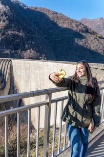 A young woman captures a selfie on a sunny winter day at the Contra Dam in Verzasca, situated in