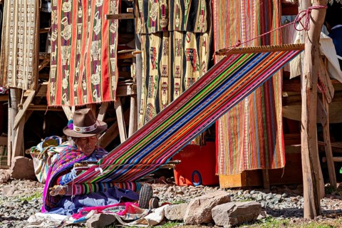 Man weaving on a colorful loom against a background of colorful fabrics, elderly traditionally