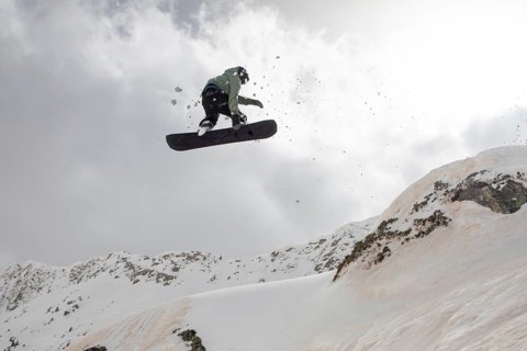 A snowboarder performs a thrilling jump off a snow-covered mountain during a backcountry freeride