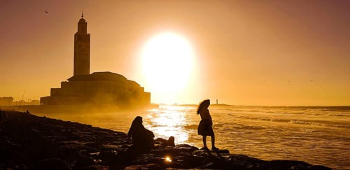 Two woman enjoying the sunset in front of the Hassan II Mosque, on a rocky beach overlooking the