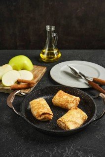 Freshly made apple crepes are served in a frying pan, accompanied by sliced green apples and