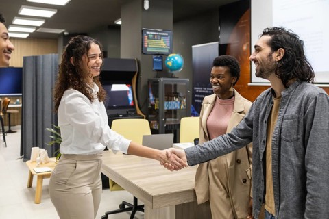 Colleagues greet each other warmly with a handshake in a modern office setting. The environment