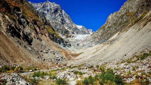 Rubble valley between high, rugged mountains under a clear, blue sky, hiking to Chalaadi Glacier,