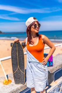 Vertical portrait of a cool young asian woman holding skateboard next to the beach