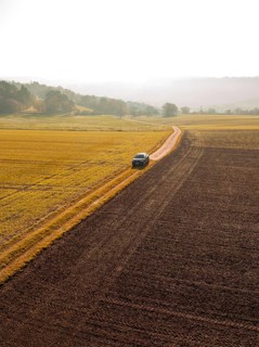 A car drives along a country lane, surrounded by autumnal fields and golden countryside, electric