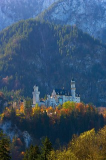 A castle lies picturesquely nestled in autumn-coloured forests against an imposing mountain