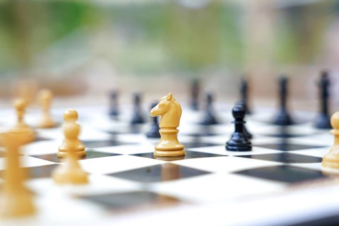 A close-up of a chessboard outside, featuring white and black chess pieces in focus The blurred