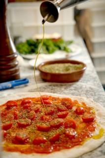Cropped unrecognizable person drizzles olive oil on a pizza base topped with tomatoes and spices on