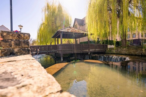 A wooden bridge crosses a river under a sunny pasture, Aidlingen, Böblingen district, Germany