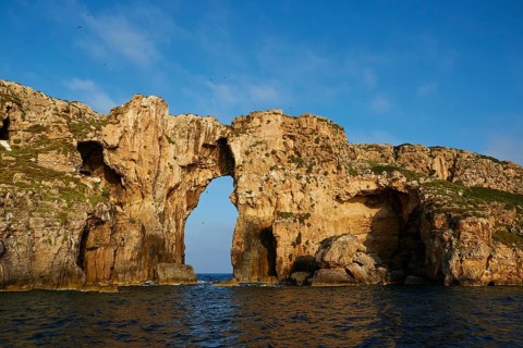 A majestic rock arch dominates the landscape, surrounded by blue sea under a clear sky, morning