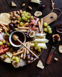 A rustic wooden board laden with an enticing variety of snacks including cheeses, grapes, figs, and