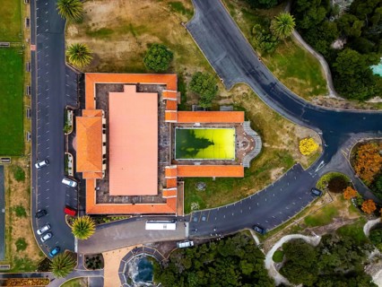 Aerial view of a unique geothermal pool with vibrant color next to a red-roofed building, roads,