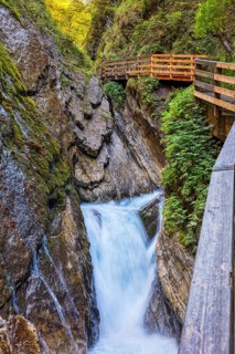 A narrow waterfall runs through a rocky gorge with a plank path nearby, awakening the spirit of