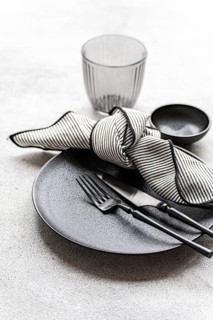 Black and white table setting featuring a textured plate, striped napkin, sleek cutlery, and a