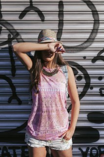 A fashionable woman poses against an urban backdrop, wearing a summer outfit with a hat and