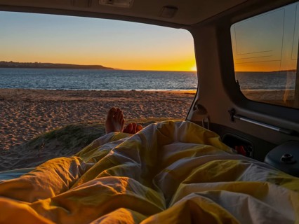 The photo captures a serene sunrise view from inside a camper van in Phillip Island, Australia. A
