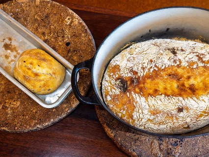Two loaves of freshly baked bread presented in a rustic setting. One loaf is in a round pot while