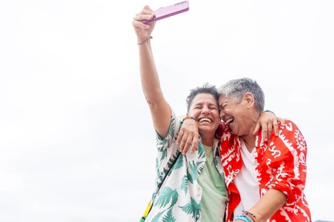 Two joyful lesbians in tropical shirts laugh and take a selfie, sharing a moment of joy during