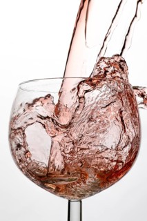 Splashing pink liquid fills a wine glass in a dynamic movement
