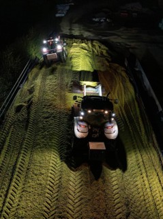 Two tractors working at night with their headlights switched on in a rural field, maize harvest,