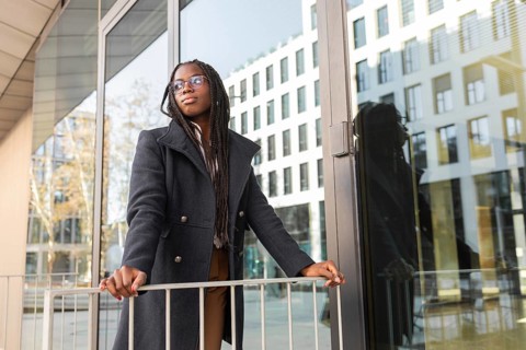 A thoughtful young African American businesswoman with braids enjoys a break outside a modern