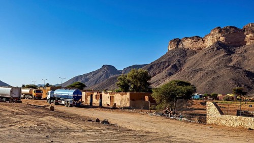 Lorry on a road in front of a mountain landscape in dry surroundings, settlement in the Sahara in