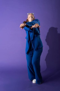 A young woman in a vibrant blue outfit dances gracefully against a vivid purple background. Her