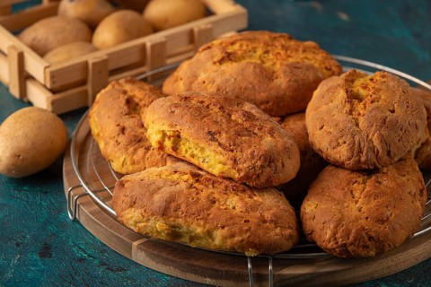 Freshly baked potato rolls with golden brown crust on a wooden board, potatoes in the background