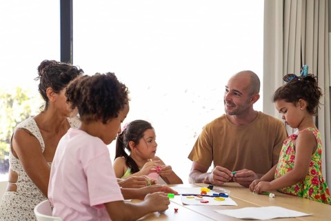 A family gathering around a table, engaging in creative activities with children. Bright setting,