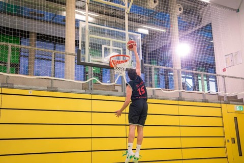 A player performs a dunk in a yellow gym in good light, basketball TSV Calw, Germany